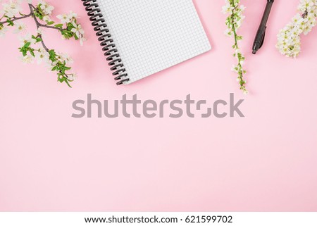 Frame of spring white flowers, notebook and pen on pink background. Flat lay, top view. Feminine workspace background.