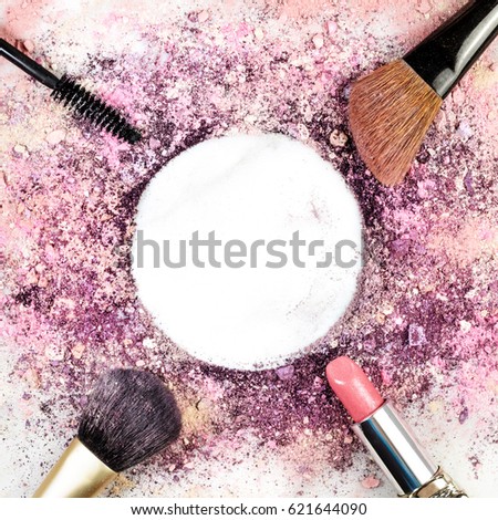Makeup brushes, lipstick, and mascara applicator on white marble background, with traces of powder and blush forming frame. Square template for makeup artist's business card, with copy space