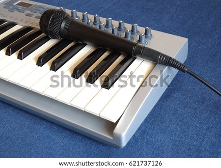 Black microphone on electronic synthesizer keyboard with many control knobs on denim background side view closeup