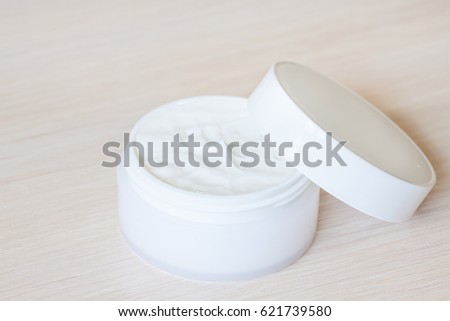 Facial and body skin care cream in white cosmetics jar with opened cap on wooden table.