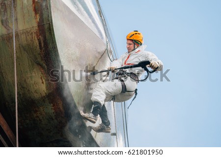 Industrial climber washing big barrel with water pressure. Risky job. Royalty-Free Stock Photo #621801950