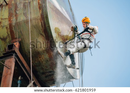 Industrial climber washing big barrel with water pressure. Risky job. Royalty-Free Stock Photo #621801959