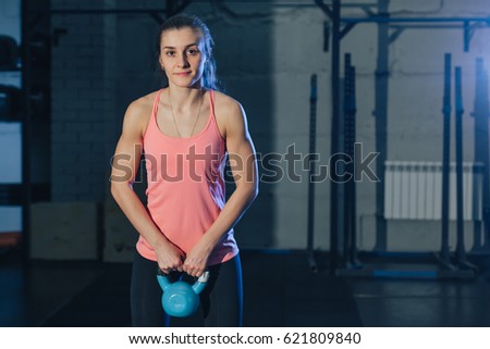 Athletic woman exercising with kettle bell while being in squat position.