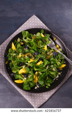 Mango, blueberries and cheese salad with pumpkin seeds on black plate. View from above, top studio shot
