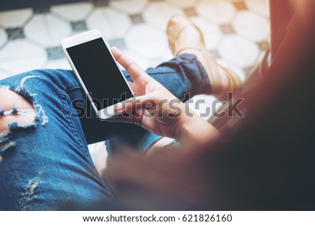 Mockup image of hand holding white mobile phone with blank black screen on leg with a vintage tile floor in cafe , feeling relax