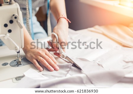 pattern, scissors, tape measure, and a sewing machine. Workplace of seamstress. Dressmaker cuts dress detail on the sketch lines. Royalty-Free Stock Photo #621836930