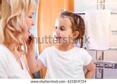 Happy loving family. Mother and daughter are doing makeup and having fun. Mother and daughter sitting at dressing table and looking at the mirror. Mom does makeup to her daughter
