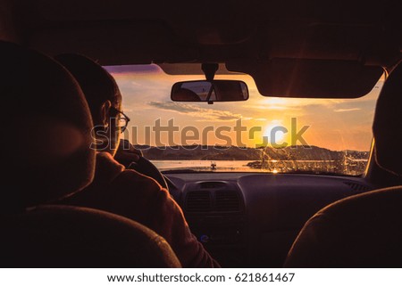 Man in car with sunset ahead.