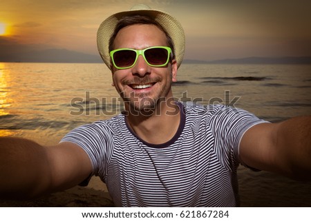 Tourist guy taking selfie on the beach at sunset  