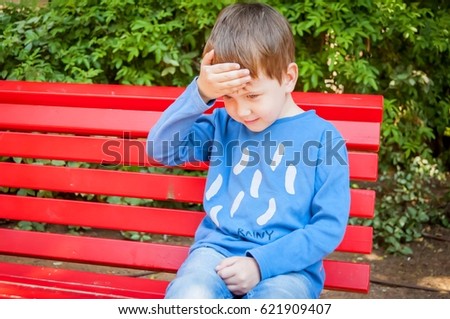 Cute optimistic Caucasian child puts a hand on his forehead as if he has a head ache stock image.