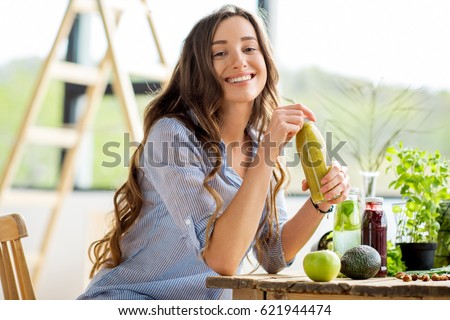 Beautiful happy woman sitting with drinks and healthy green food at home. Vegan meal and detox concept Royalty-Free Stock Photo #621944474