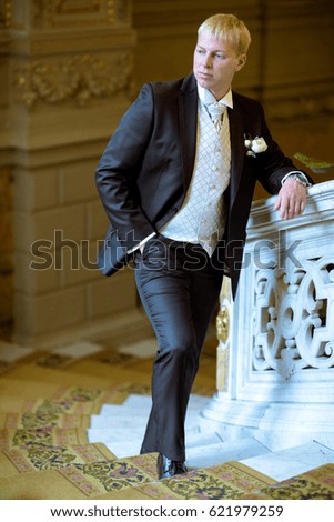 Handsome groom in suit in the hall. Male portrait in the room. Beautiful model boy in colorful wedding clothes. Man is posing. Handsome guy indoors