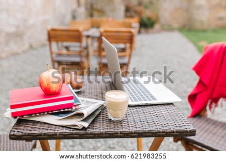 Wooden table with a glass of milk shake, red apple and white computer. Daily newspapers and books next  to morning latte, croissant and laptops. Workplace, freelance