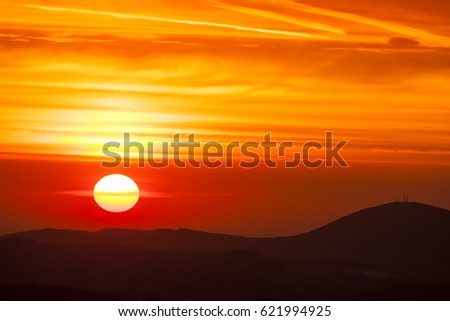 Natural Sunset Sunrise Over Highland or Mountains. Bright Dramatic Sky And Dark Ground. Countryside Landscape Under Scenic Colorful Sky At Daybreak Dawn. Sun Over Skyline, Horizon. Warm Colors.