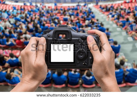 Hand holding the camera over Top view of Abstract blurred photo crowd of spectators on a stadium with a football match, sport background concept