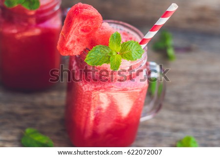 Healthy watermelon smoothie in Mason jars with mint and striped straws on a wood background.