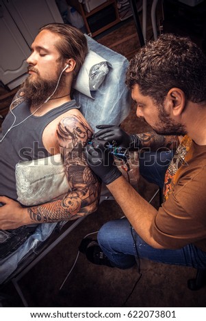 Professional tattooer makes tattoo pictures in tattoo parlor./Professional tattooist doing tattoo in salon.