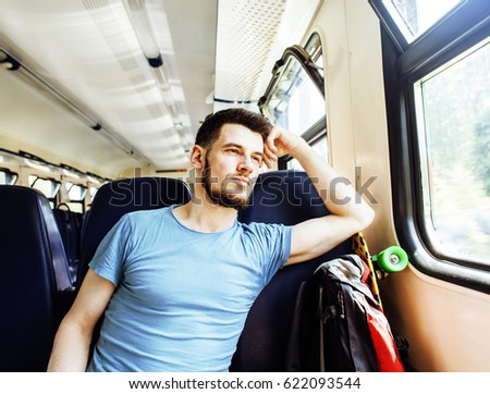 young pretty modern hipster guy traveller on train with skateboard alone, lifestyle vacation people concept close up smiling cool
