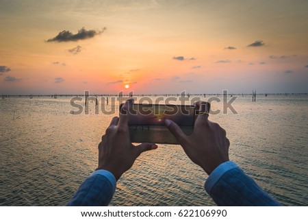 Woman using smartphone to take photo at sunset time on lake