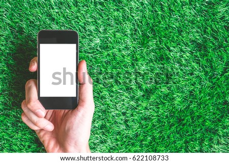 Male hand holding smart phone on green grass background. Free space for text