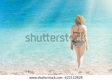 Woman in a swimsuit standing near the sea in the sunlight, view from the back