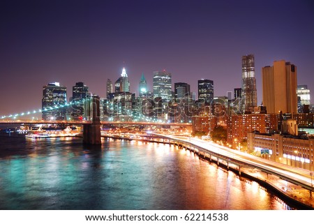 New York City Manhattan skyline and Brooklyn Bridge with skyscrapers over Hudson River illuminated with lights and busy traffic at dusk after sunset.