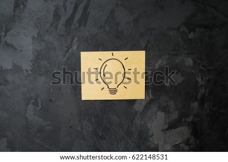 drawing of lightening bulb on a sticky note paper on abstract concrete wall