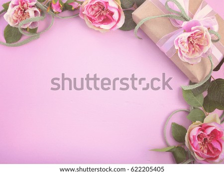 Pink feminine background with gift and silk roses on wood table with decorated borders, for Mothers Day, Valentine, birthday or anniversary with copy space, with applied vintage style filters.