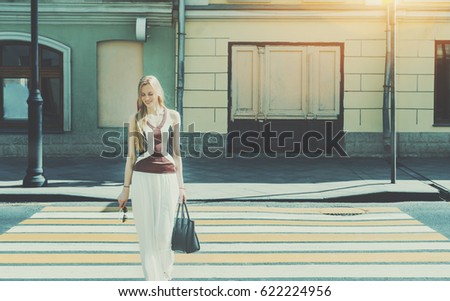 Smiling tall beautiful adult woman passing crosswalk on summer springtime, cheerful blonde lady with bag on pedestrian crossing with copy space for advertising, logo or your text