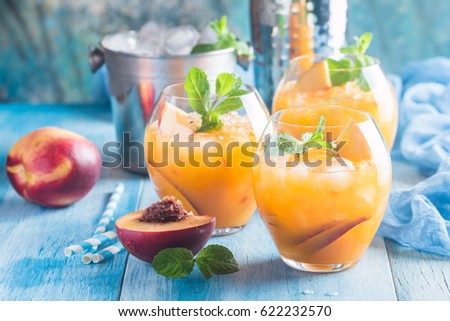 Peach cocktail or tea with ice and mint on blue background.