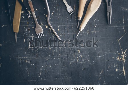 Leather craft tools on a wooden background. Leather craftmans work desk . Piece of hide and working handmade tools on a work table.with copyspase