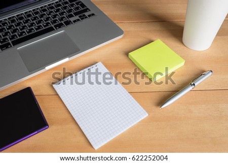 Laptop with paper cup, smartphone, pen and notepad with message on wooden desk. Morning workspace in office