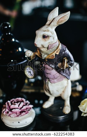 Table decor. Alice in wonderland. Figure of a rabbit with clock stands behind black bowl