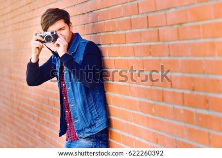 Young and handsome guy stands by a brick wall and takes pictures on a mirrorless camera