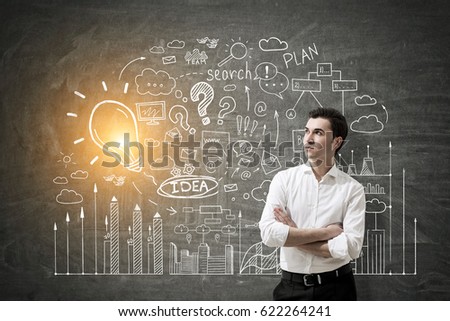 Portrait of a young confident businessman standing with crossed arms near a blackboard with a business idea sketch on it.