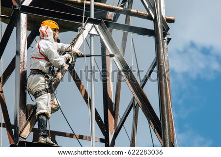 Industrial climber washing big barrel with water pressure. Risky job. Royalty-Free Stock Photo #622283036