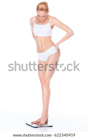 Young slim woman in underwear standing on digital scales and looking down on white