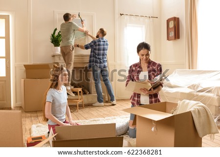 Young women opening boxes with books while male friends hanging picture on wall 