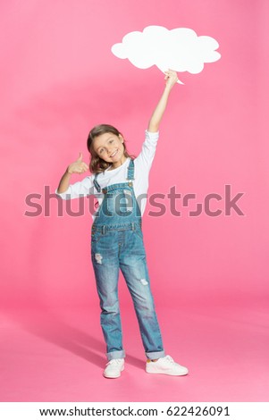 Adorable smiling little girl holding blank speech bubble and showing thumb up