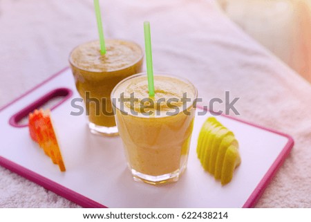 Two smoothies of apples, pears, oranges, bananas, stand on the white Board drink
