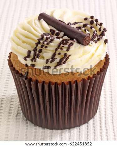 SINGLE SPONGE CUPCAKE WITH CREAMY FROSTING AND CHOCOLATE ON WHITE