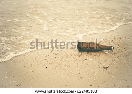 empty glass bottle lying on the sand beach with sea wave water. picture with copy space. vintage photo and film style.