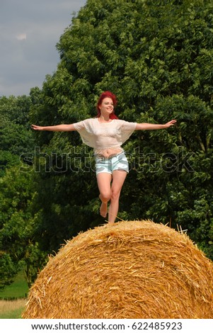 A beautiful young red headed girl dances on a row of hay bales.
The young girl has an expression of happiness and joy on her face.
