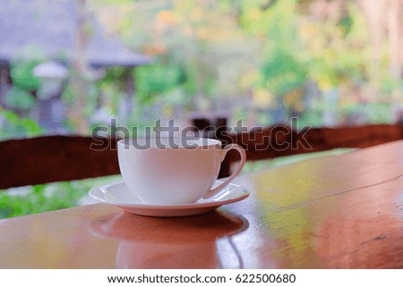 a selective focus picture of a cup of coffee on wooden table in green garden 