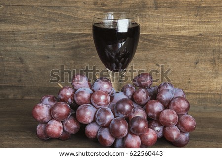glass of red wine and red grapes on wooden background