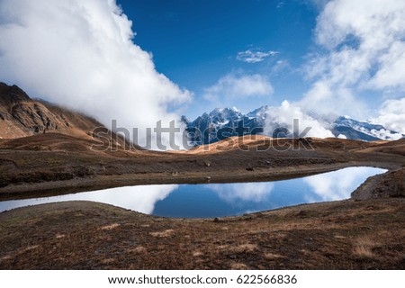 Rocky ridge covered with snow reflecting in the Koruldi lake. Majestic view with clouds floating through the mountains. Upper Svaneti region, Georgia, Europe.