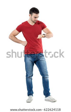 Young upset casual man waiting for someone checking time on wrist watch. Full body length portrait isolated over white studio background. Royalty-Free Stock Photo #622624118