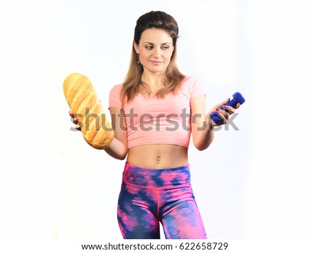 Sports lifestyle or harmful nutrition. Fitness girl holding bread and dumbbells.
