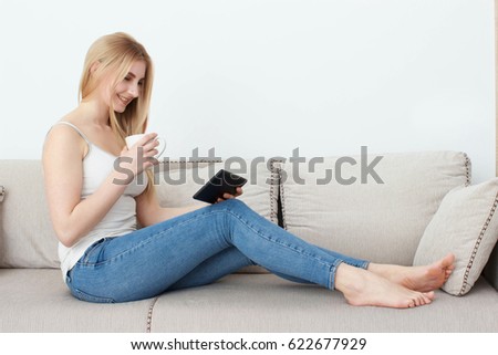 Woman in home cozy clothes sitting on a sofa using a tablet and a cup of coffee in her hands. Online education concept. e-Learning