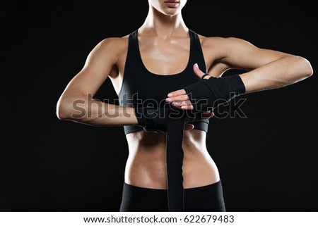 Cropped picture of young sports lady boxer standing over black background and posing.